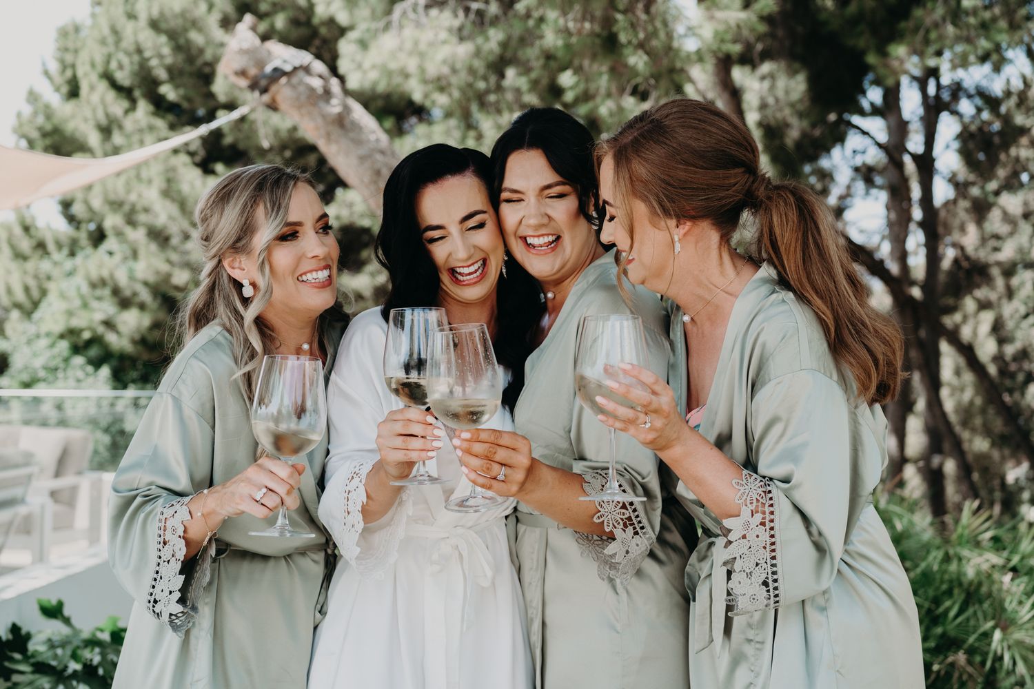 Group of women in matching sage robes laughing and toasting with champagne glasses.