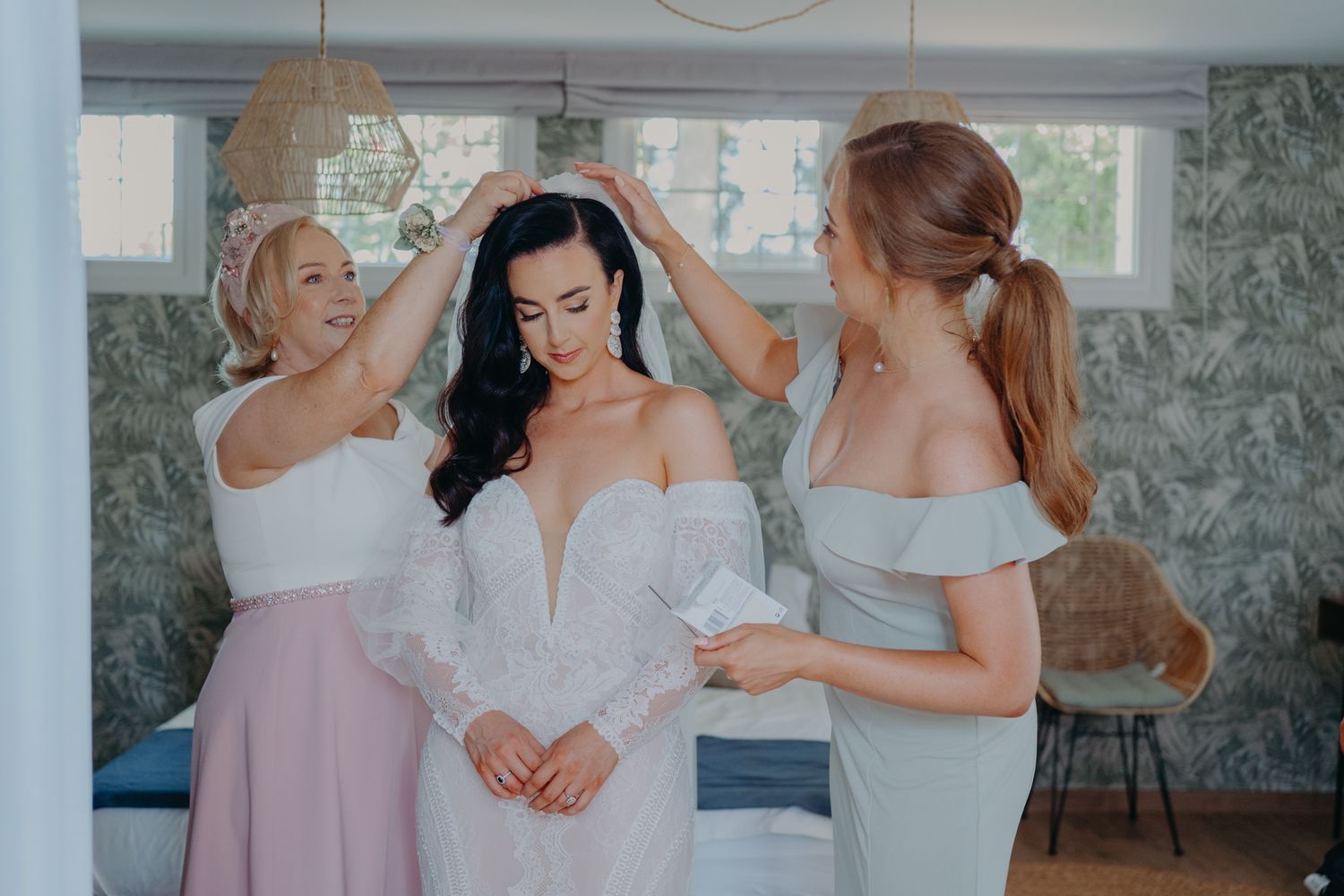 Three women help adjust a wedding dress in a light-filled room with modern decor.