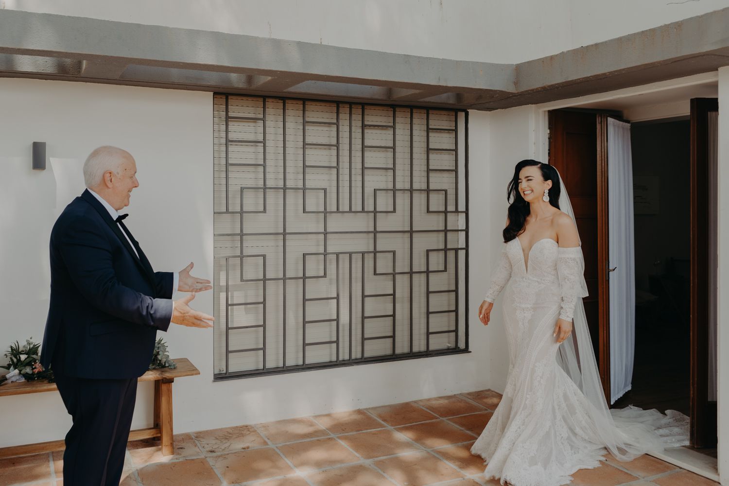 A first look moment between a bride and an older gentleman in a formal setting with geometric wall panels.