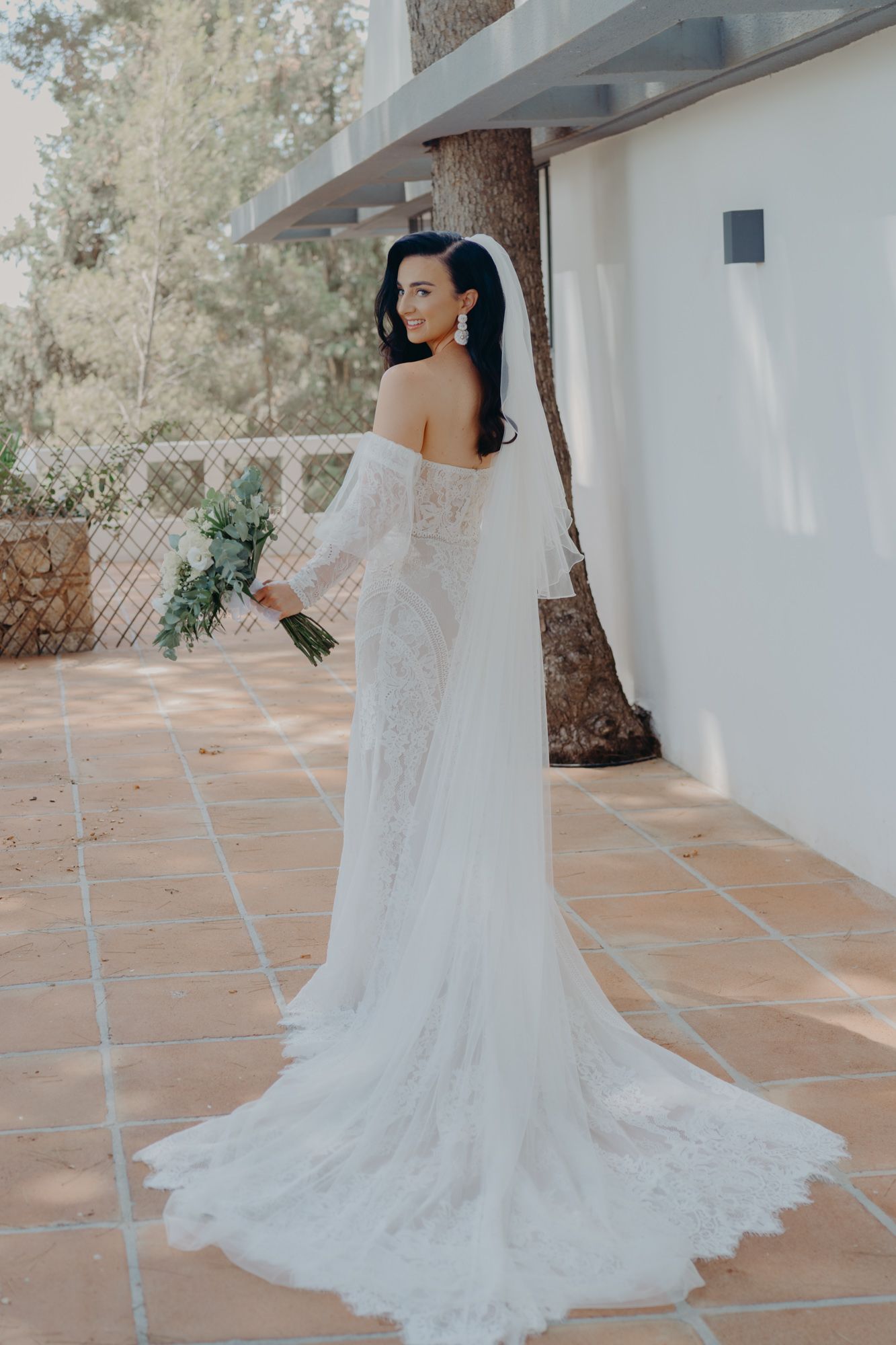 A stunning off-shoulder wedding gown with lace details and flowing train photographed from behind.