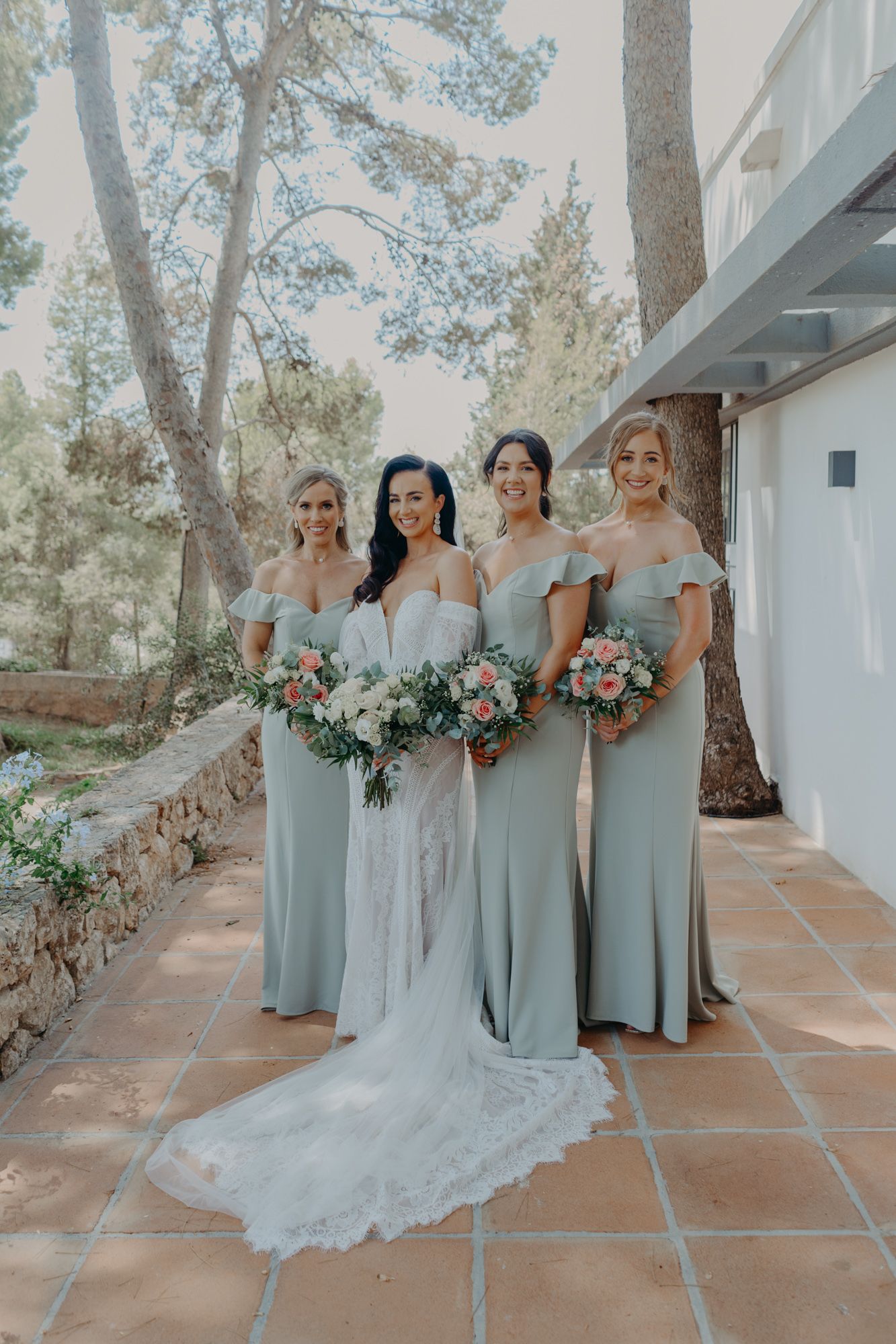 Bridal party in pale sage green dresses and white wedding gown pose together on a Mediterranean style terrace.