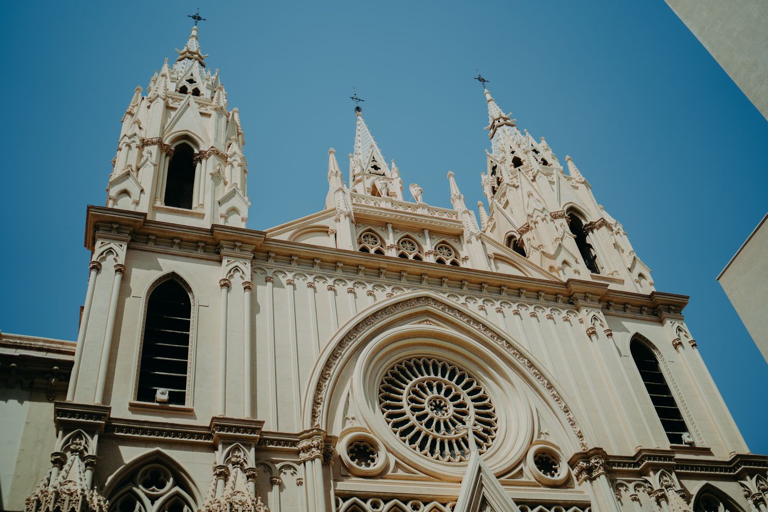 Gothic revival church facade with ornate spires and rose window against bright blue sky.