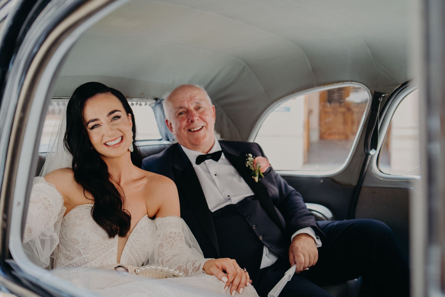 A bride and older man sharing a joyful moment in a vintage car.