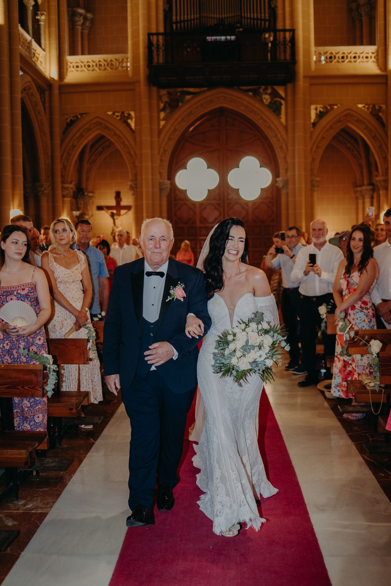 Elegant church wedding ceremony with bride walking down red carpet aisle in ornate gothic cathedral.