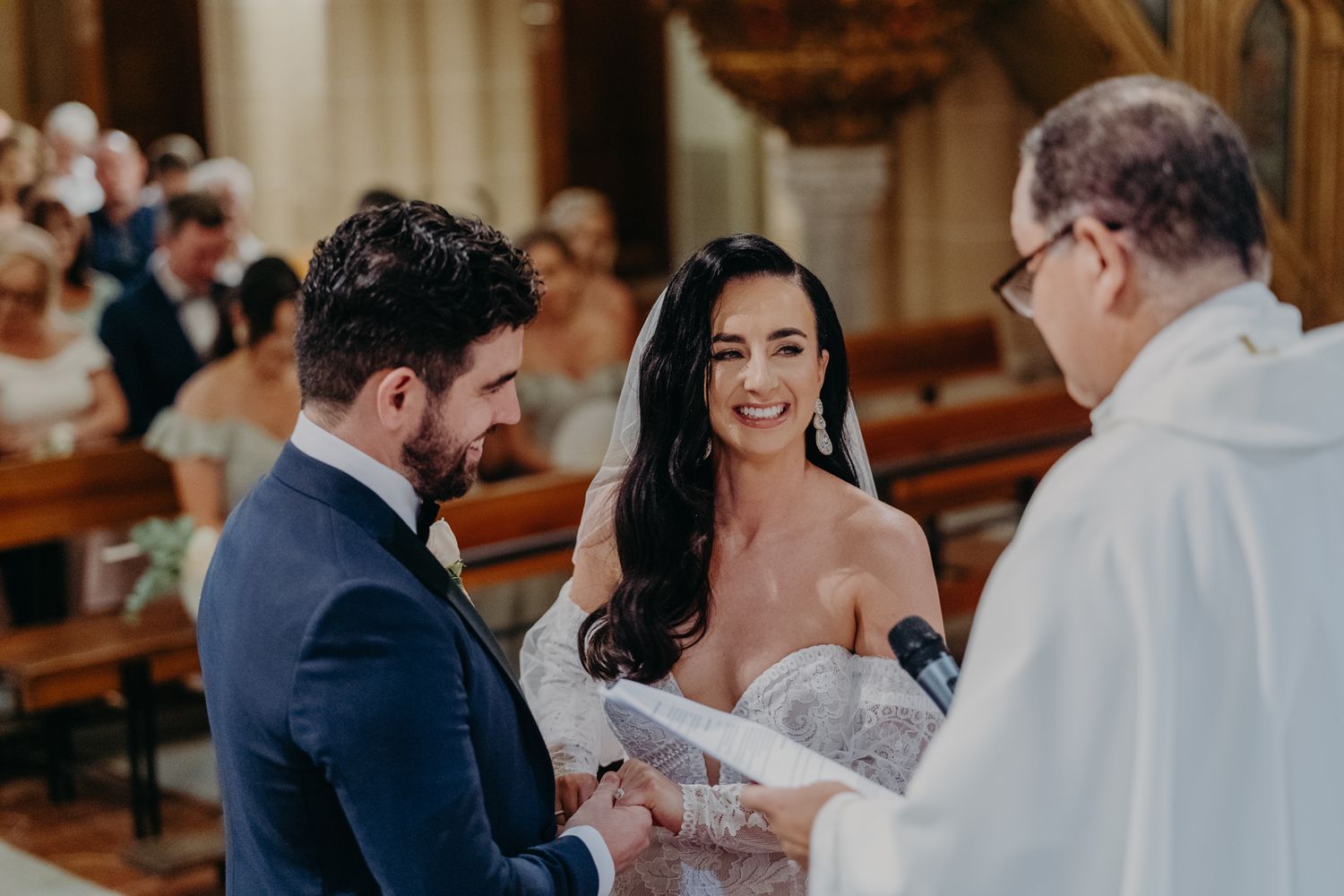 A couple exchanges rings during their wedding ceremony inside a historic church with wooden pews.