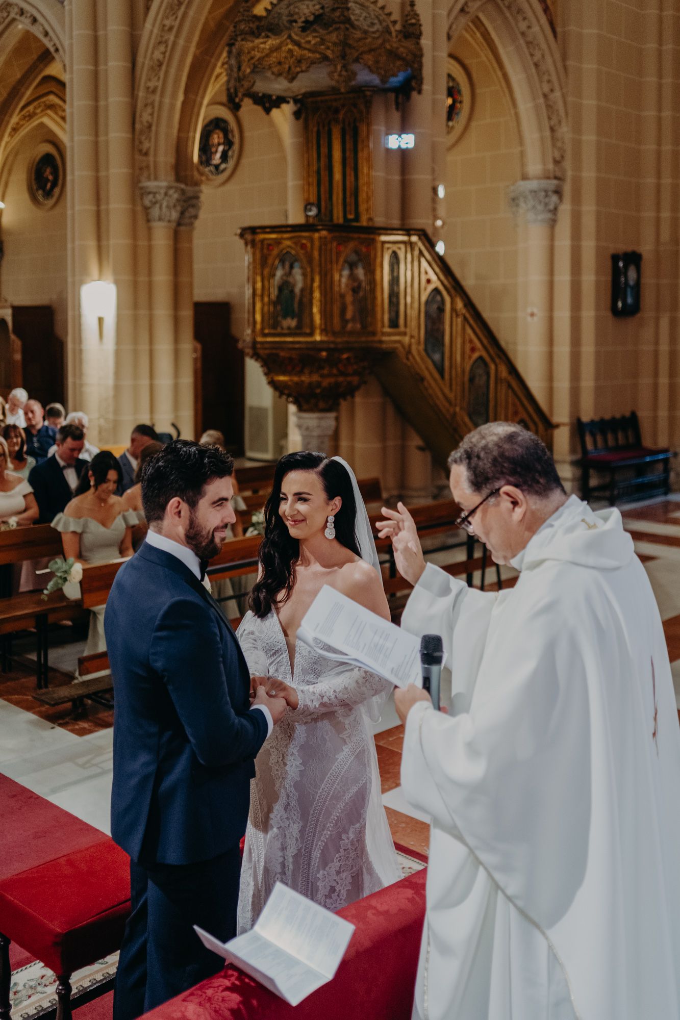 A wedding ceremony takes place in a grand cathedral with gothic architecture and wooden details.
