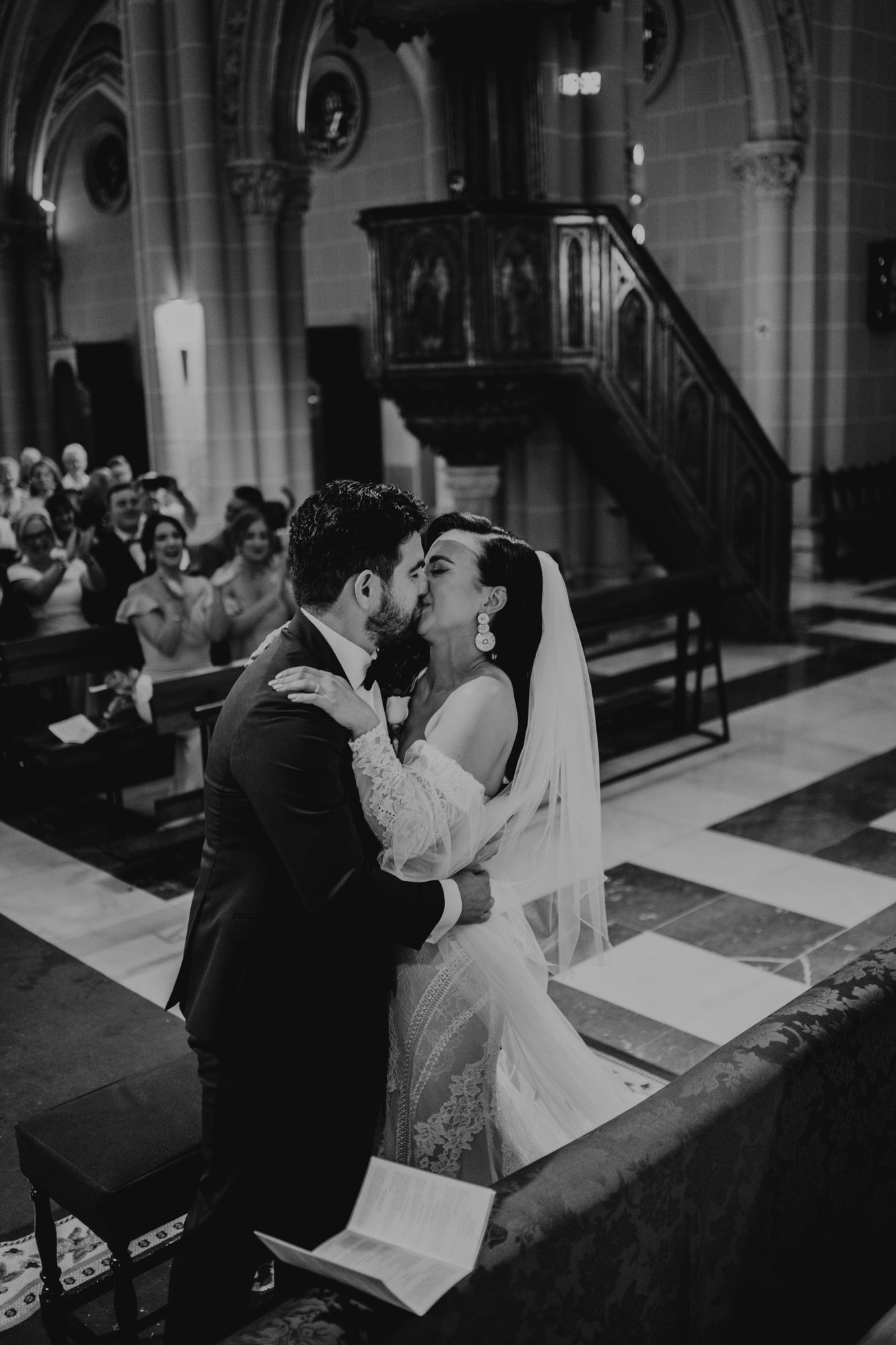 A couple shares their first kiss as newlyweds during a romantic black and white church wedding ceremony.