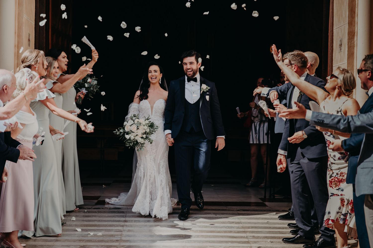 Wedding guests shower newlyweds with flower petals as they exit the church.
