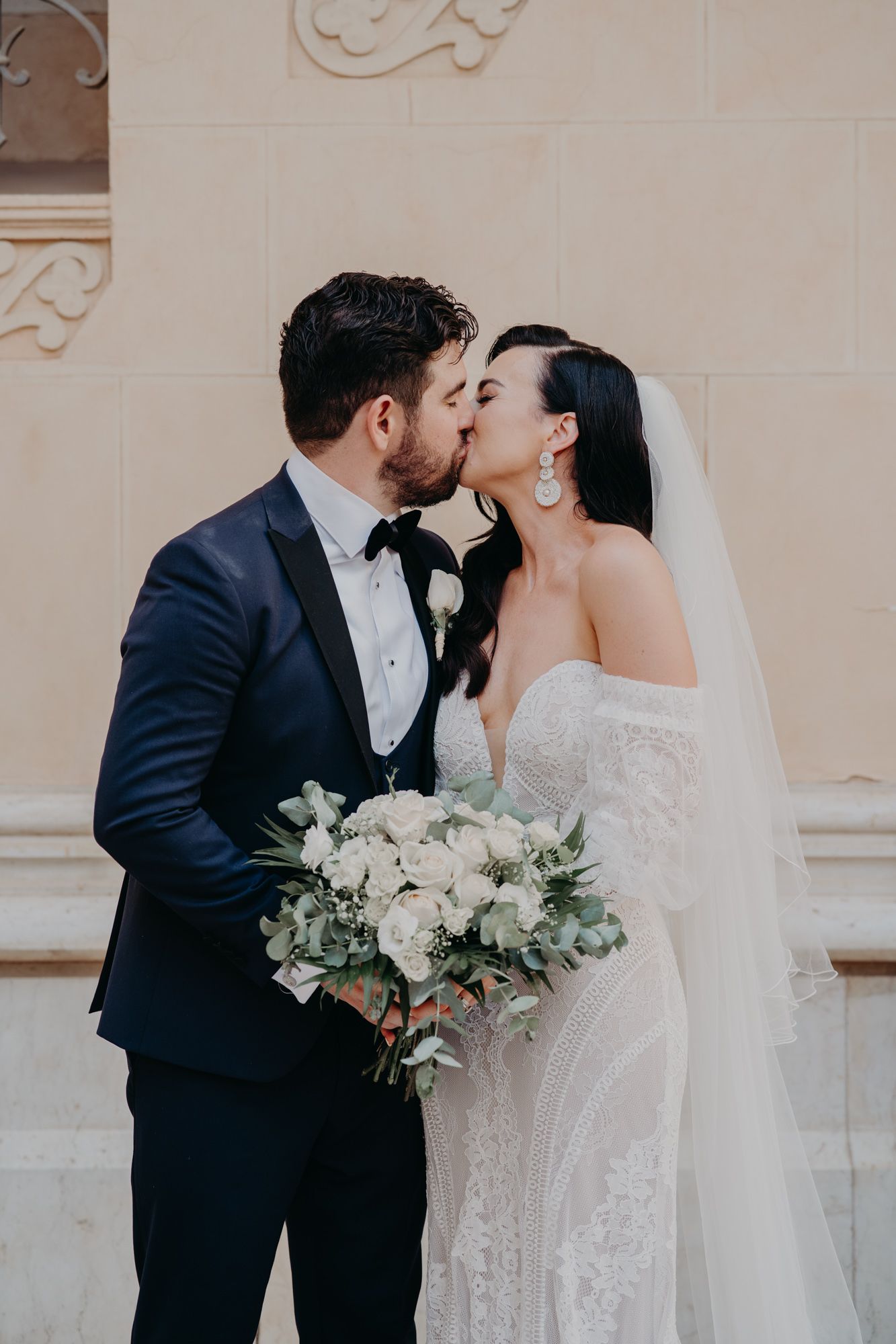 A romantic moment between newlyweds in formal attire with a beautiful white bouquet in hand.