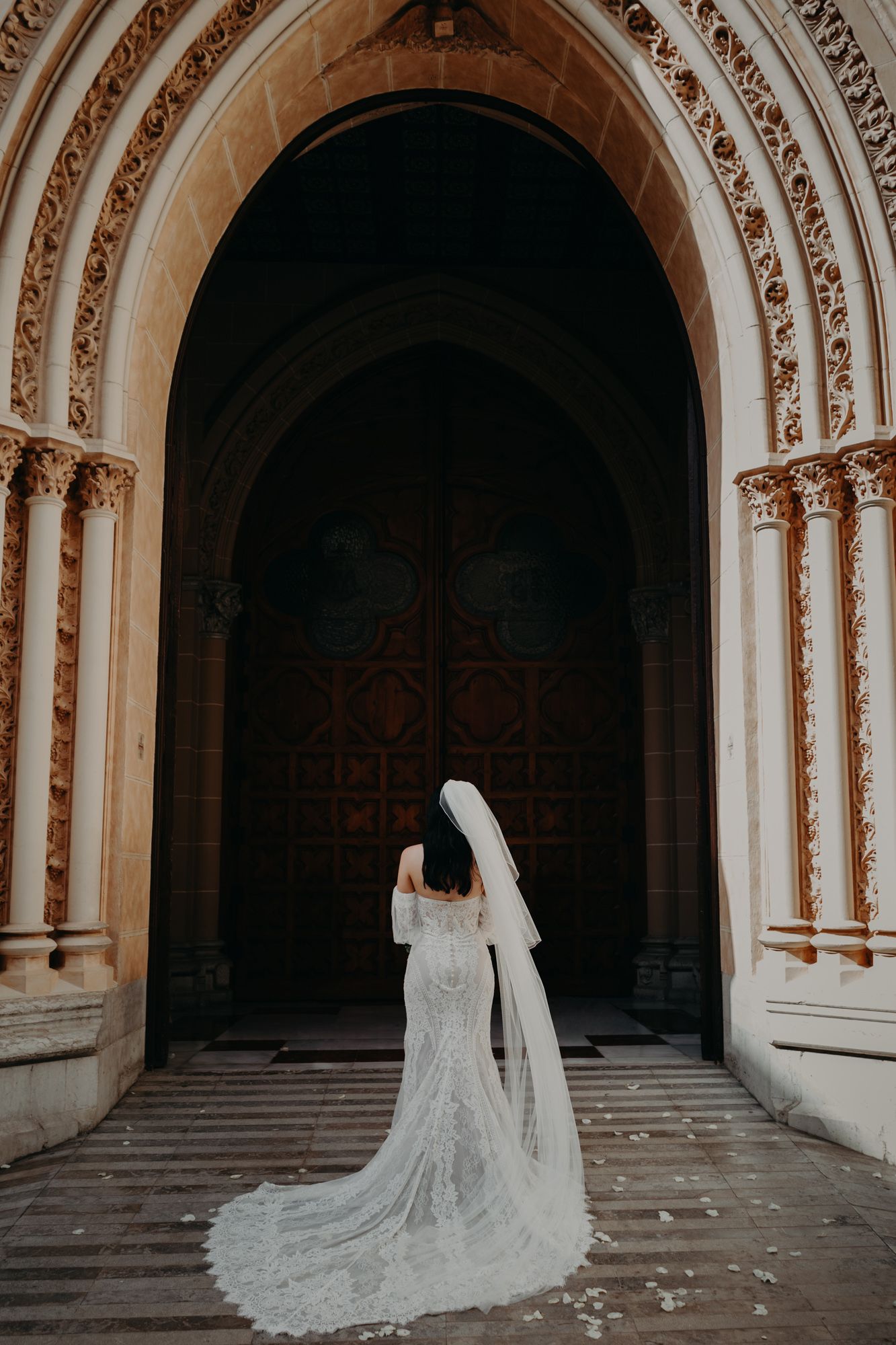 A lace wedding gown with long train and veil photographed in an ornate gothic church archway.