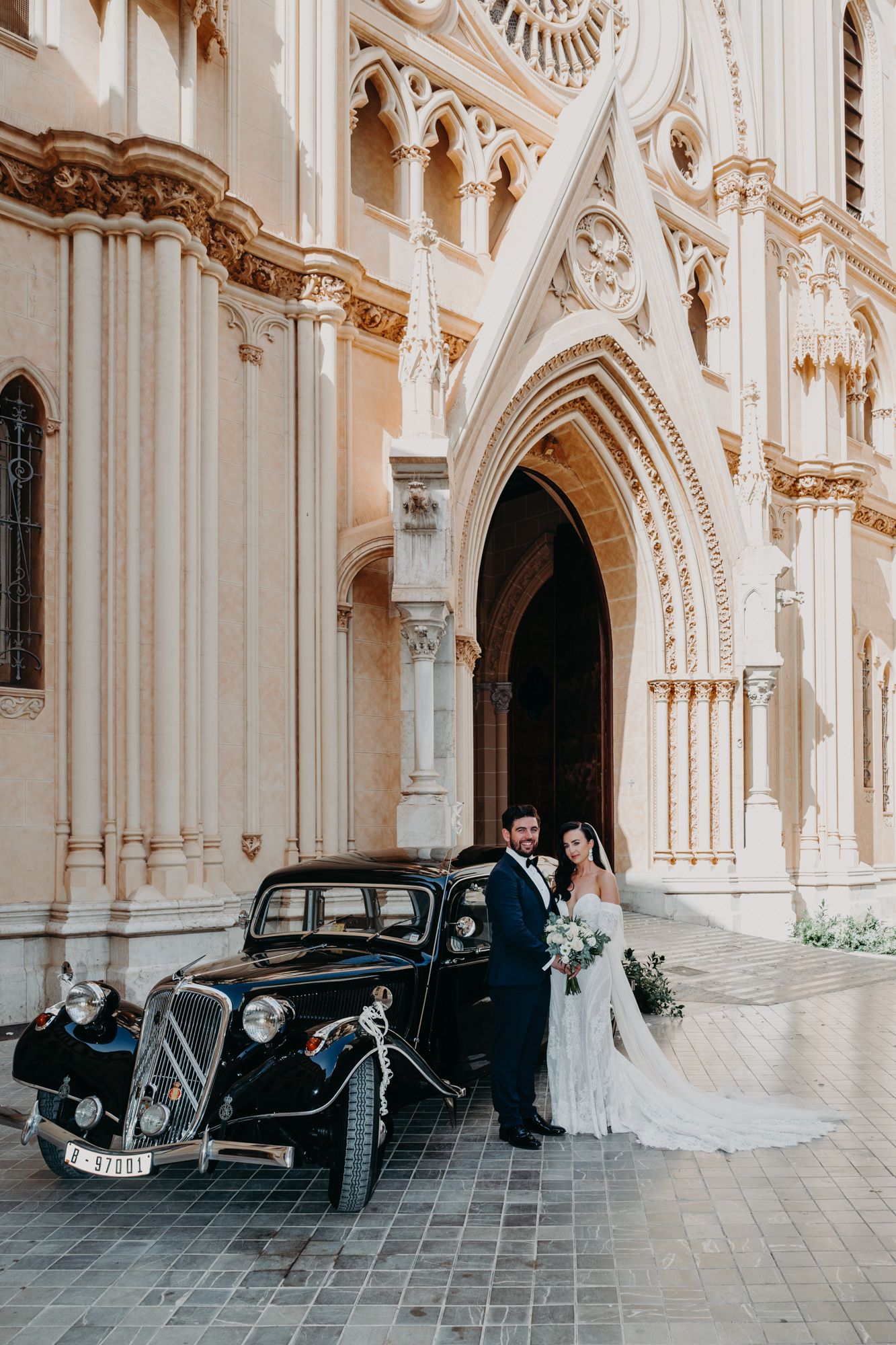 Classic vintage car parked in front of ornate gothic church facade on wedding day.