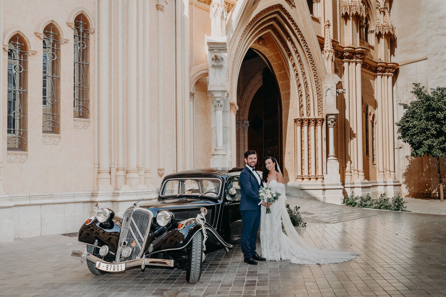 Vintage black Citroen car parked outside a gothic church entrance with wedding party.