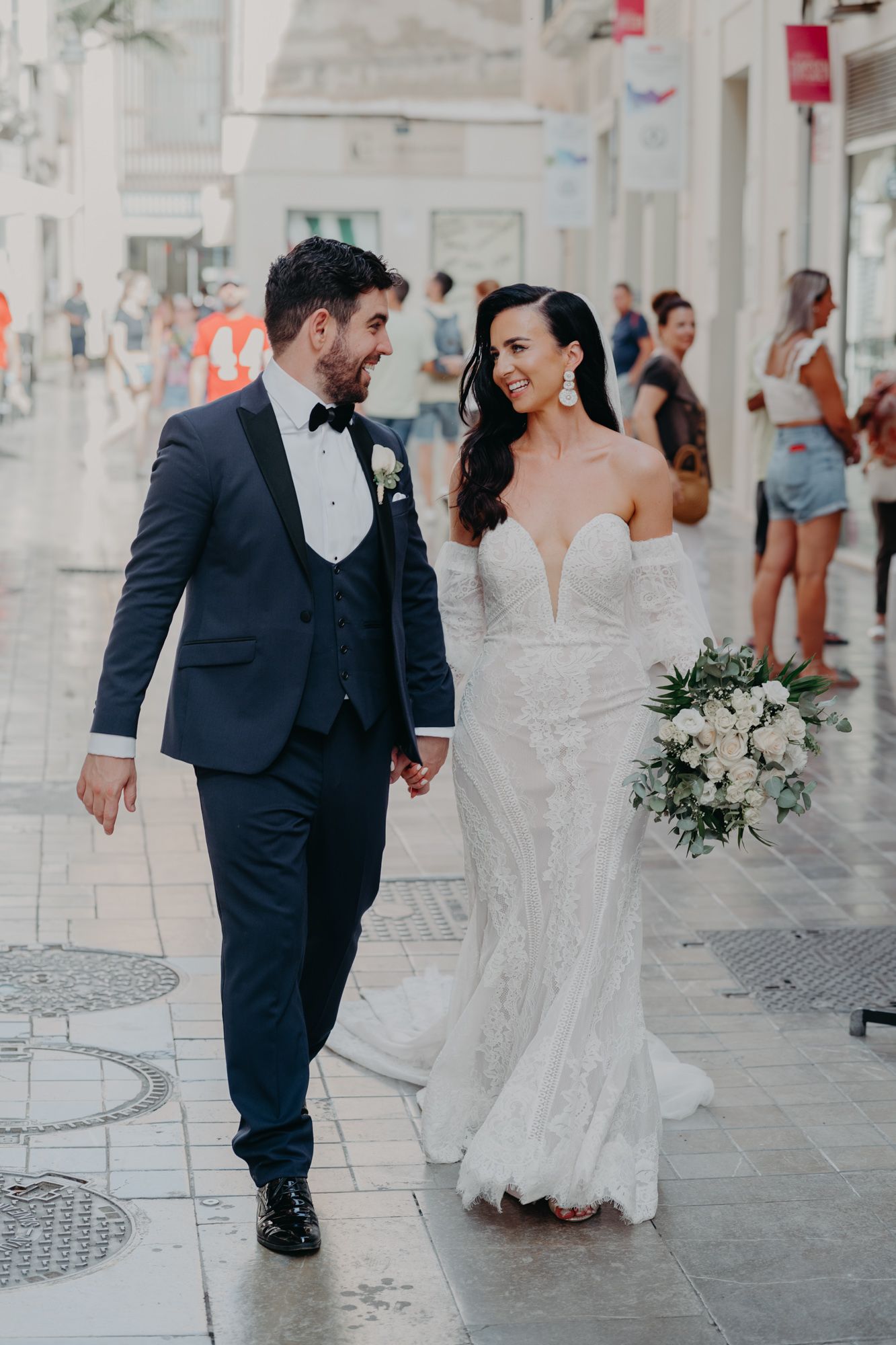 A couple in wedding attire walks along a city street after their ceremony.