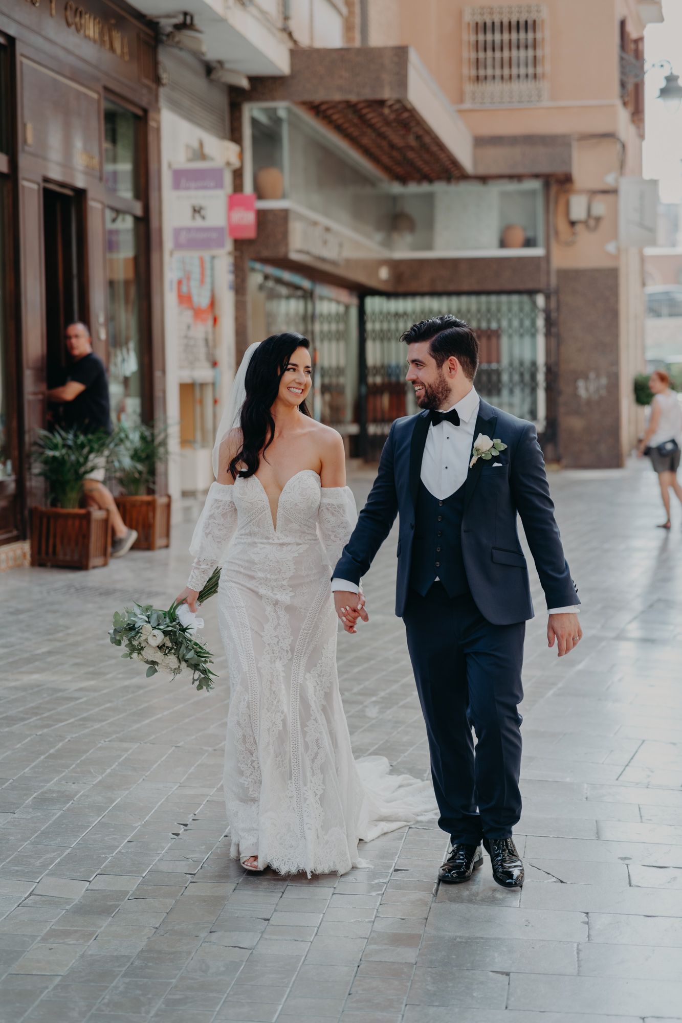 Elegant couple walking hand in hand through city streets after their wedding ceremony.