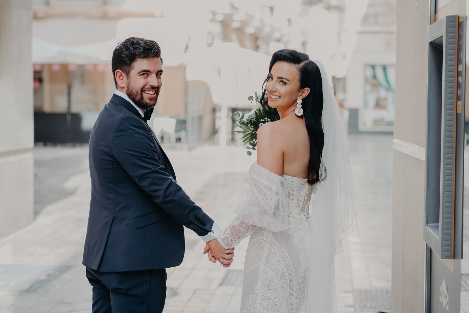A romantic wedding moment captured on a sun-lit street with white walls.