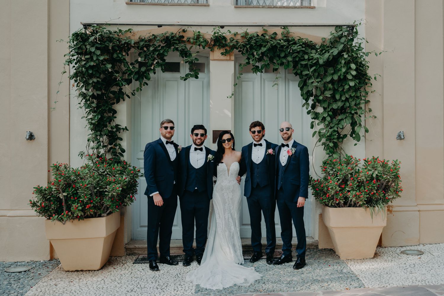 Wedding party poses in front of ivy-covered wall and elegant cream-colored doors.