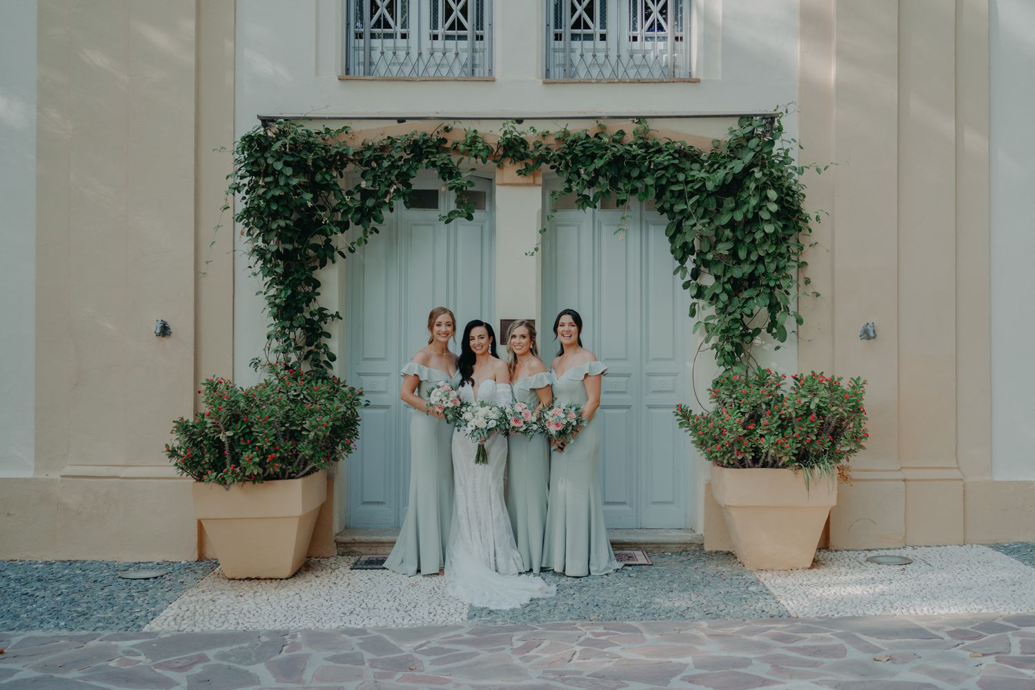 Elegant bridal party in soft blue dresses stand in front of a vine-covered wall.