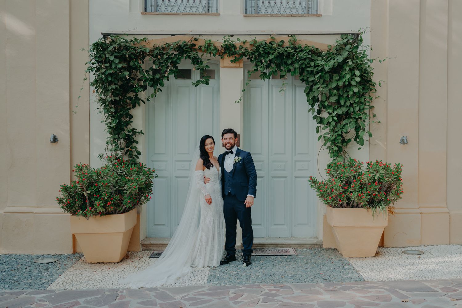 Elegant couple poses in front of cream-colored doors with climbing ivy decoration.