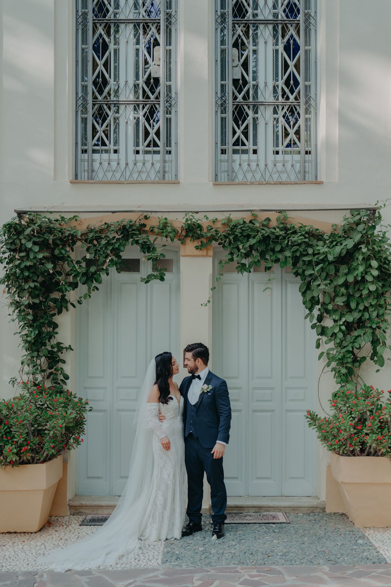 Romantic wedding portrait against light blue doors with climbing ivy and stained glass windows.