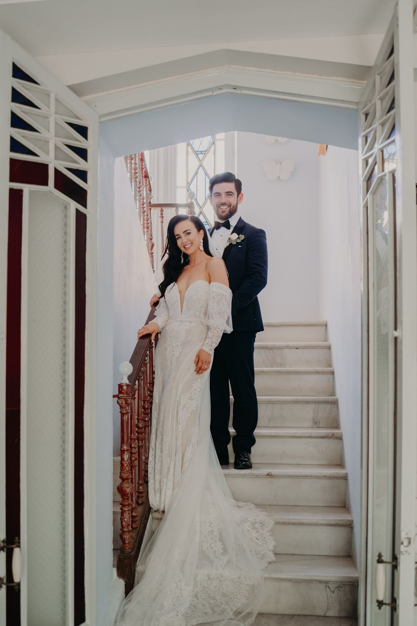 Elegant bride and groom pose together on white marble staircase during their wedding day.