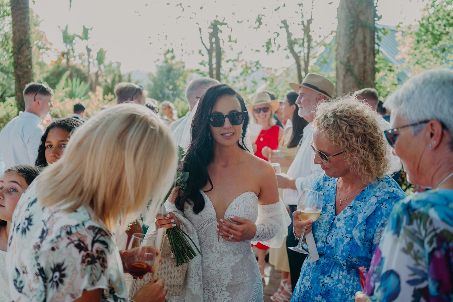 Wedding guests mingle and socialize at an outdoor reception on a sunny day.