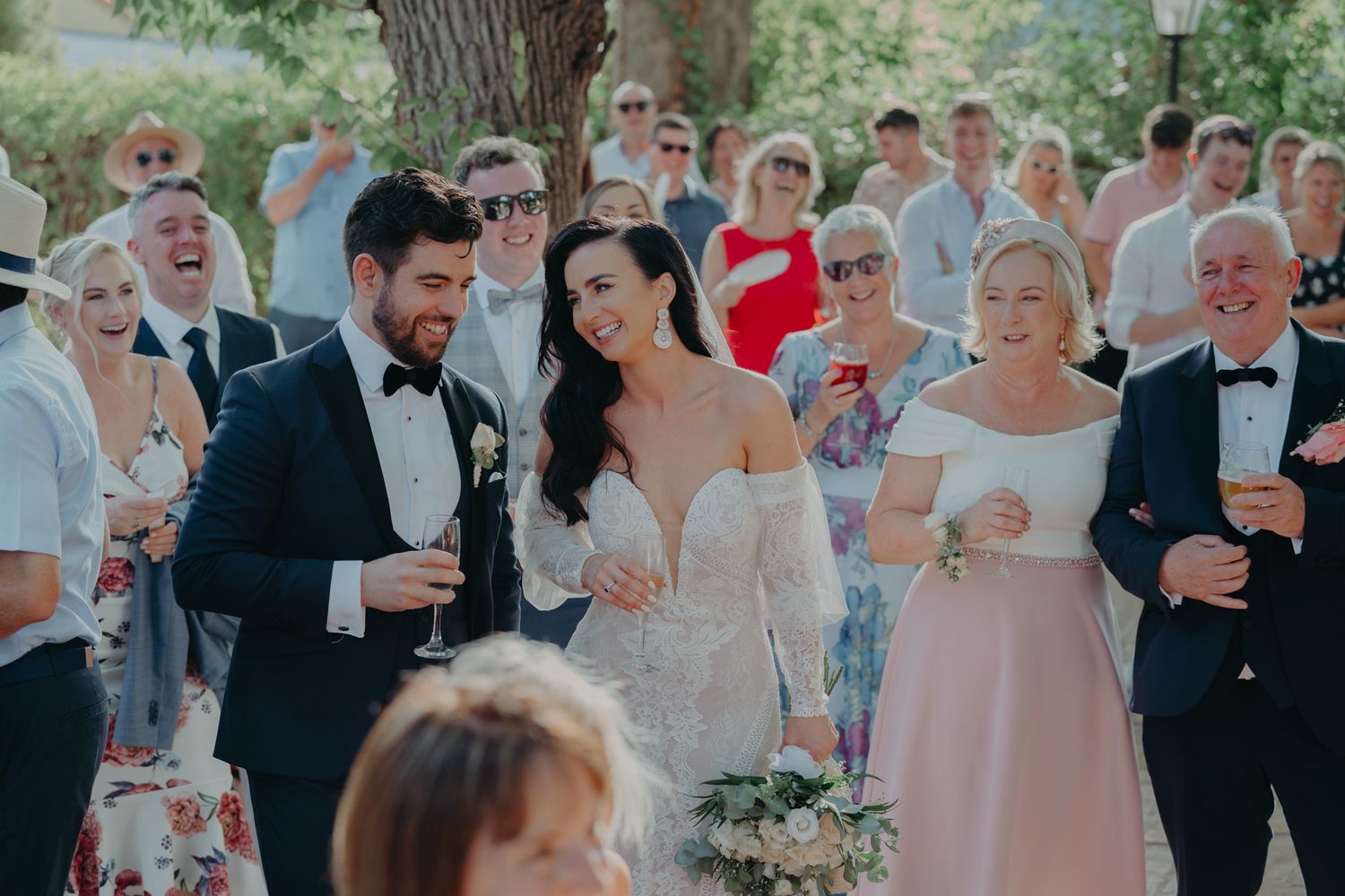 Elegant outdoor wedding celebration with guests mingling in formal attire among trees.