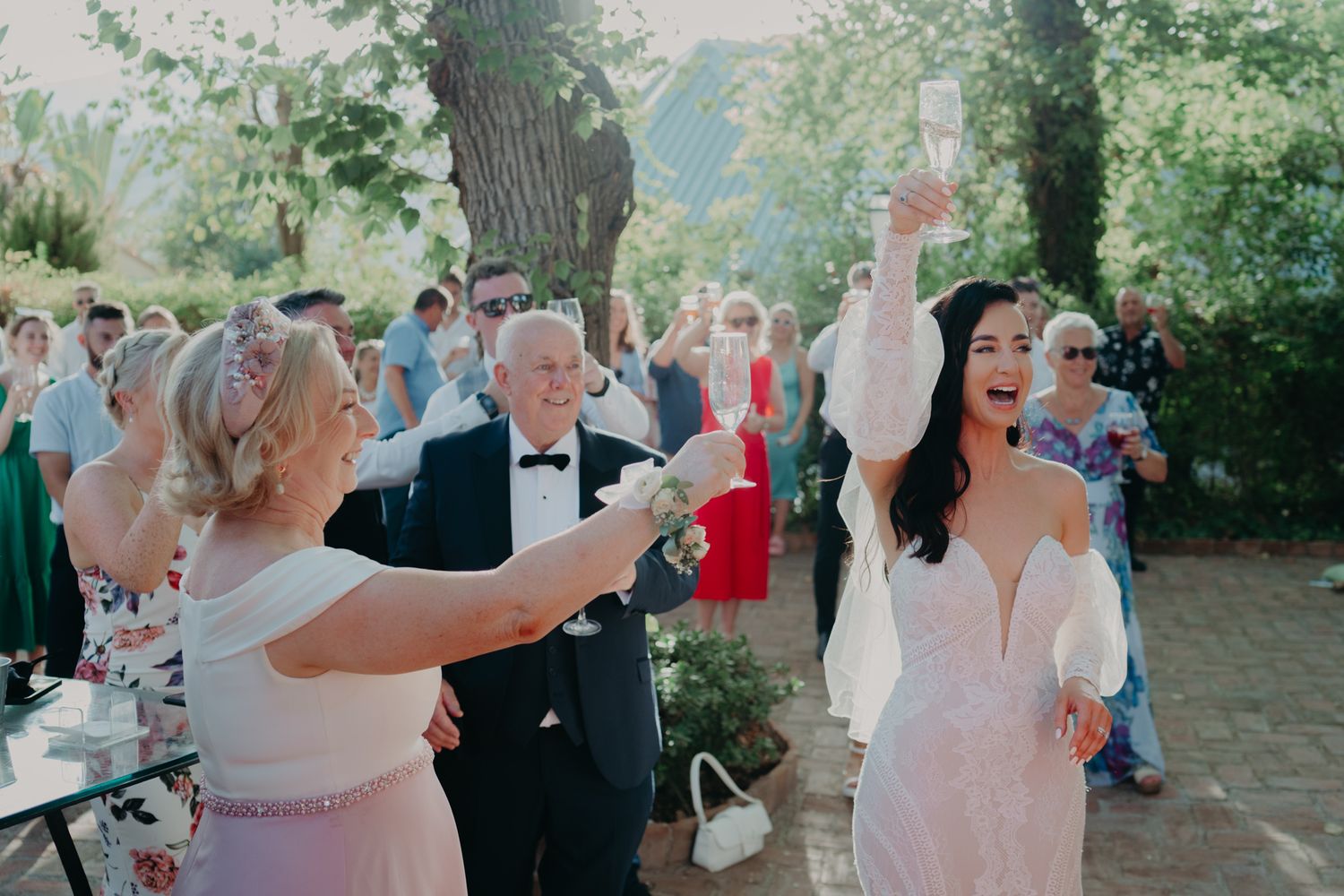 Wedding guests celebrate joyfully while dancing outdoors at a summer garden reception.