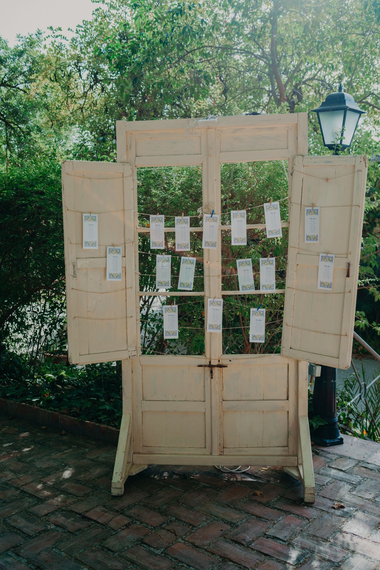 A vintage white door display with seating cards arranged for wedding guests stands against a garden backdrop.