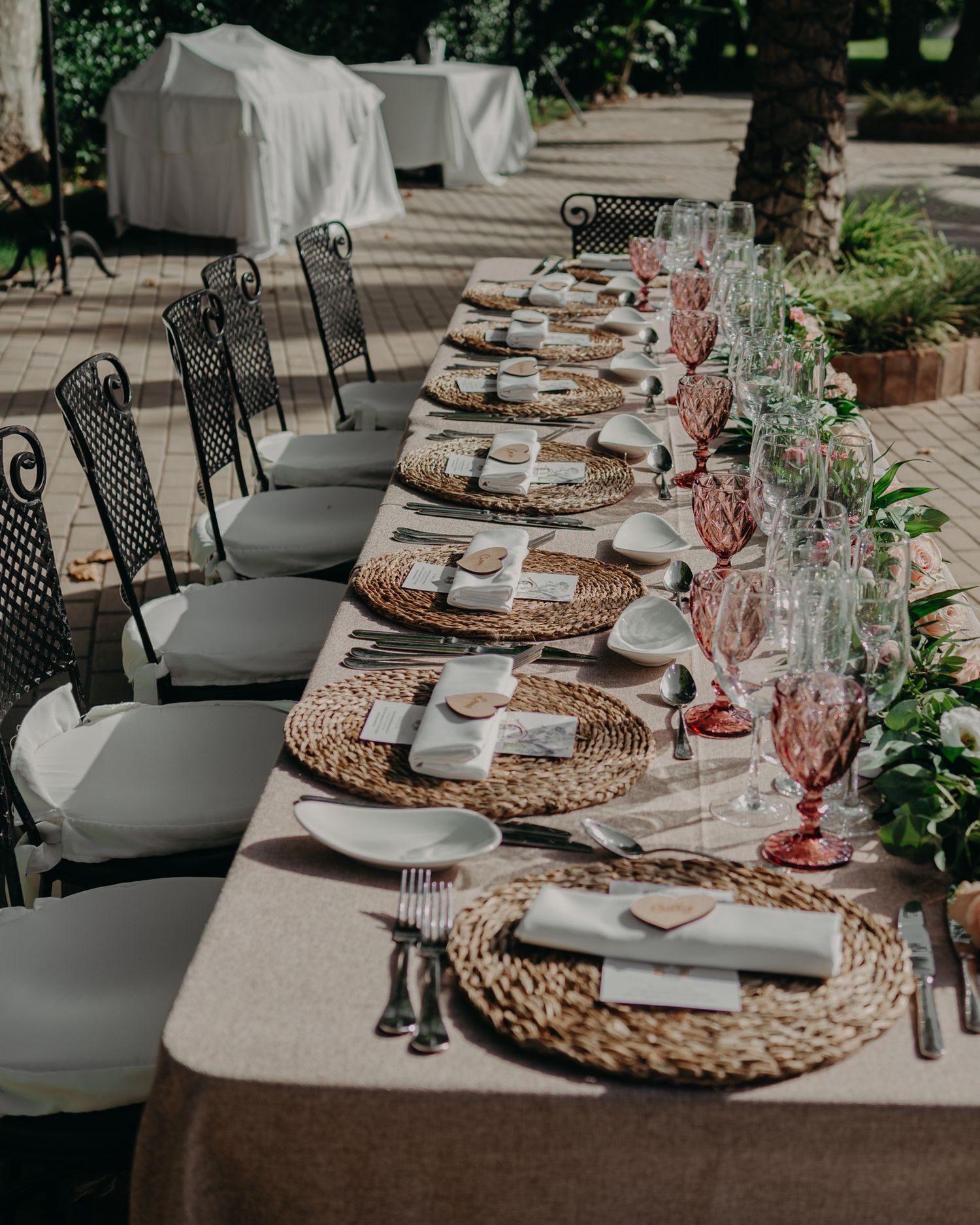 Elegantly set wedding table with wicker chargers, pink glassware, and natural garden decor.