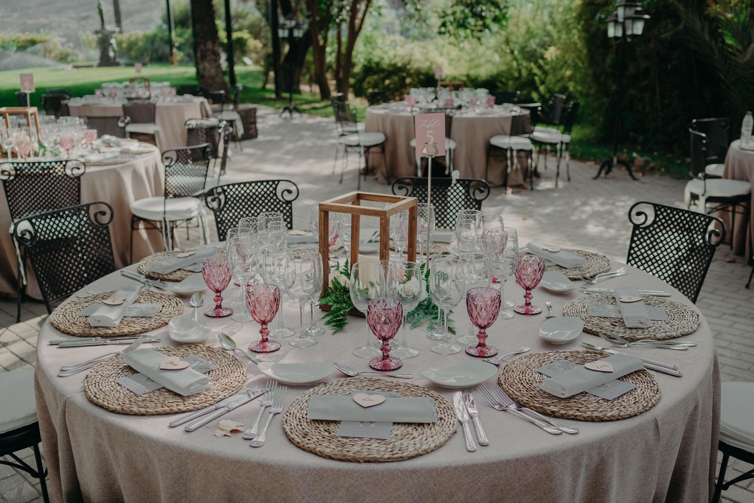 Elegant wedding table setting with pink glassware and gold charger plates on a round table.
