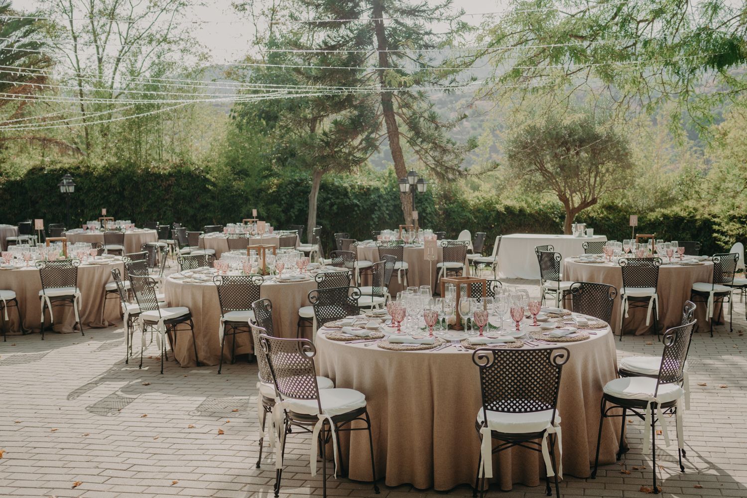 Outdoor wedding reception setup with round tables and neutral linens under a forest canopy.