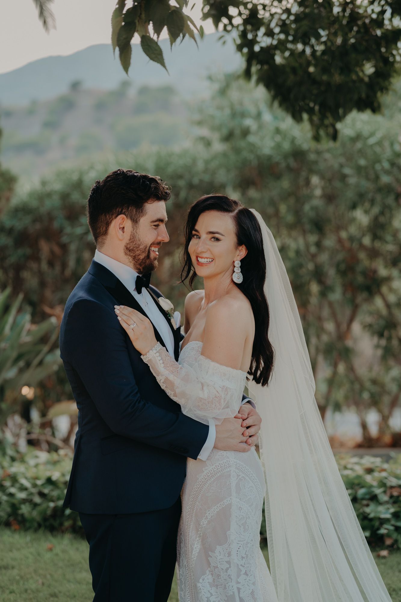 Newlyweds share an intimate moment in a garden setting with mountain views and natural lighting.