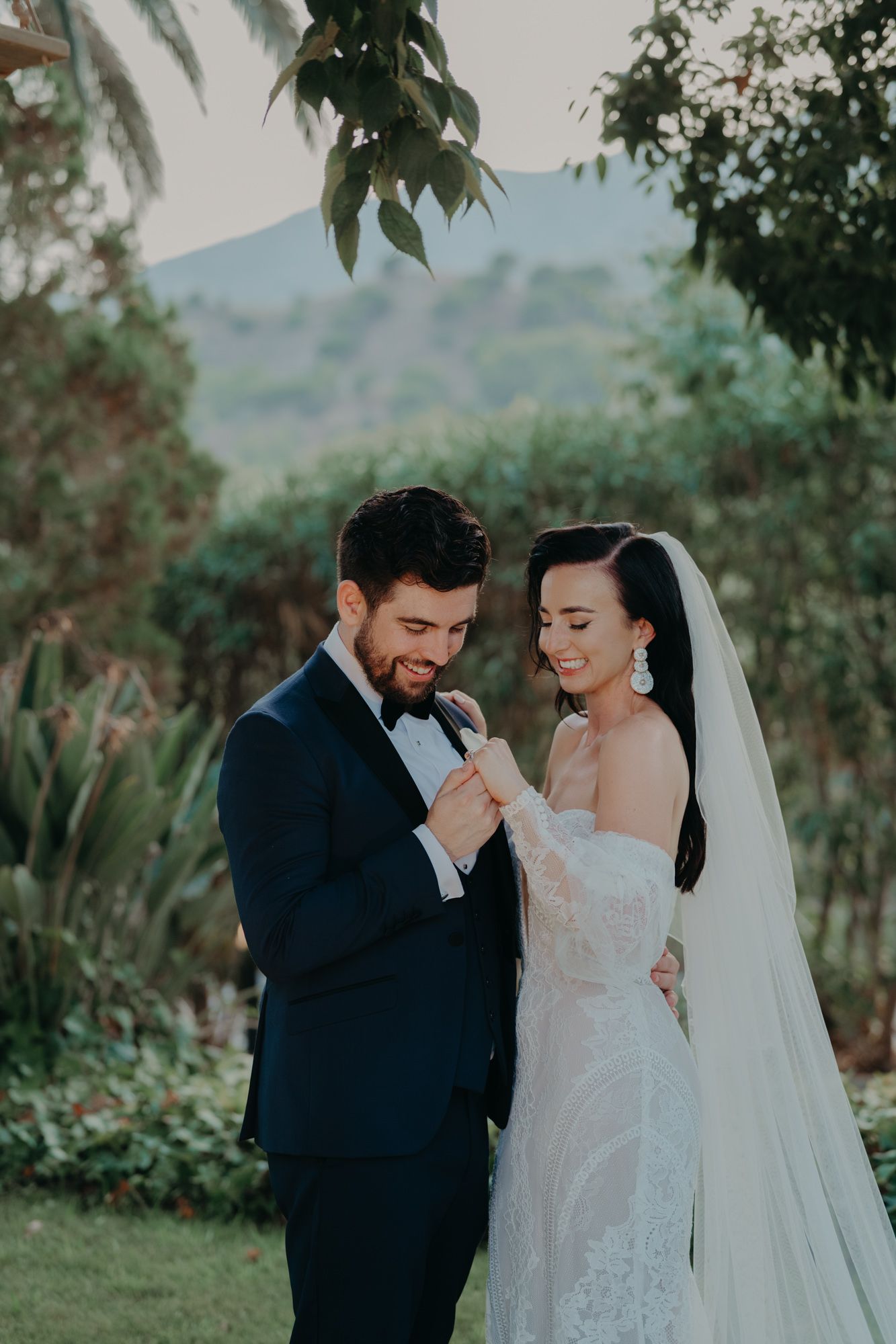 Newlywed couple shares an intimate moment outdoors with lush greenery in the background.