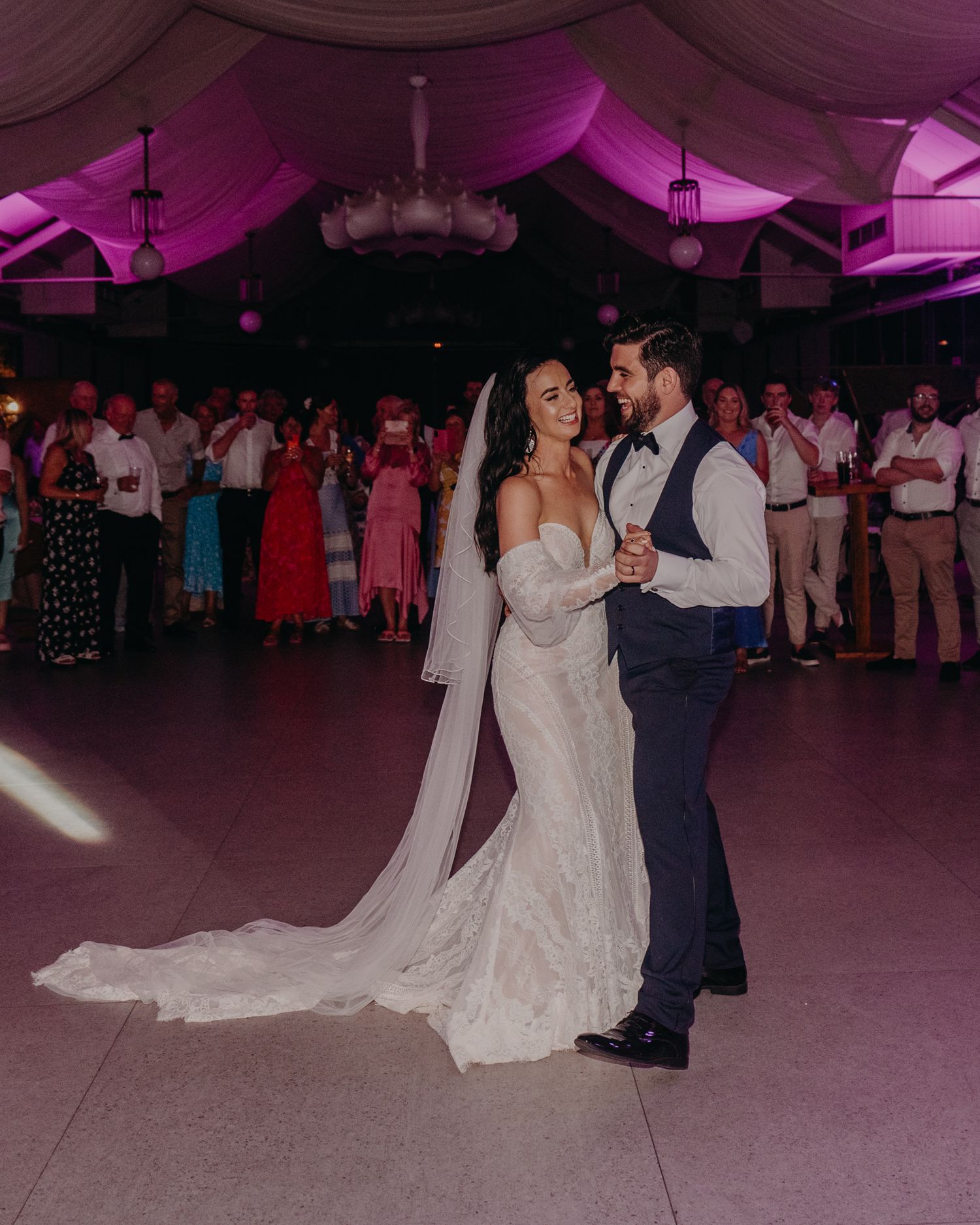 A couple shares their first dance under purple lighting in a reception tent.