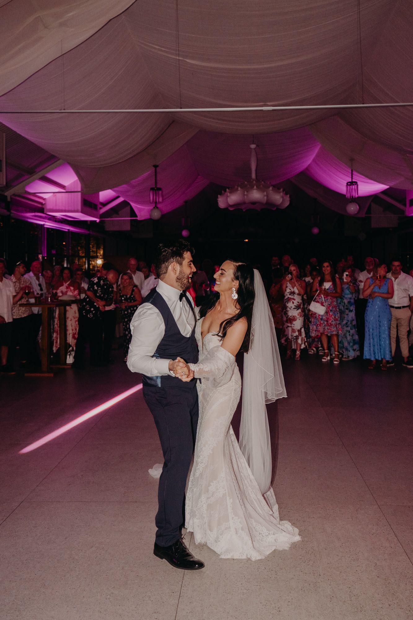 A couple dancing at their wedding reception under purple-lit tent with a lightsaber prop.