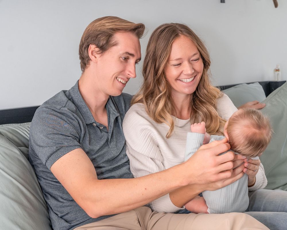 A happy couple sits on a couch at home spending quality time with their infant baby.