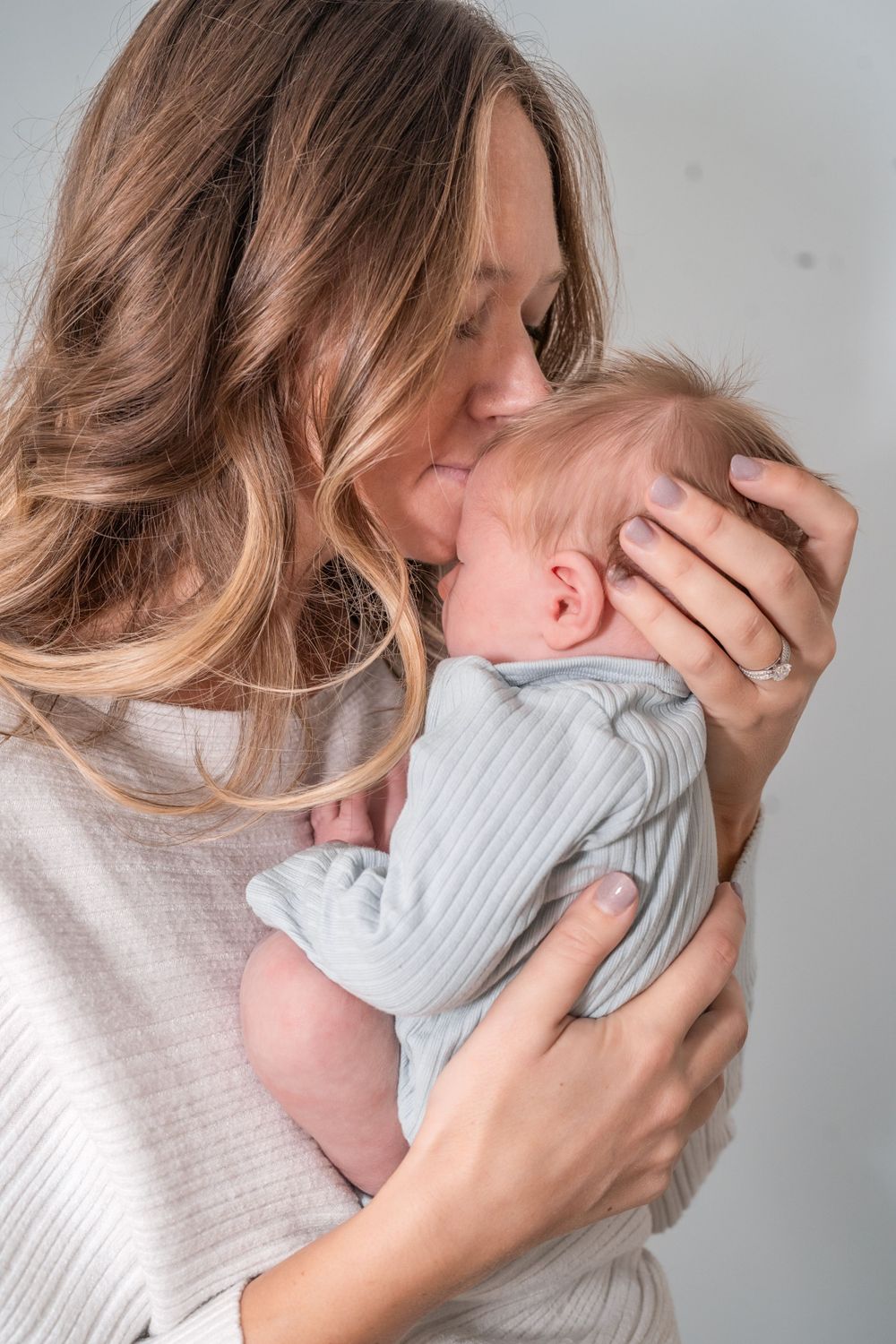 A tender moment between parent and baby as they embrace in soft natural light against a neutral background.