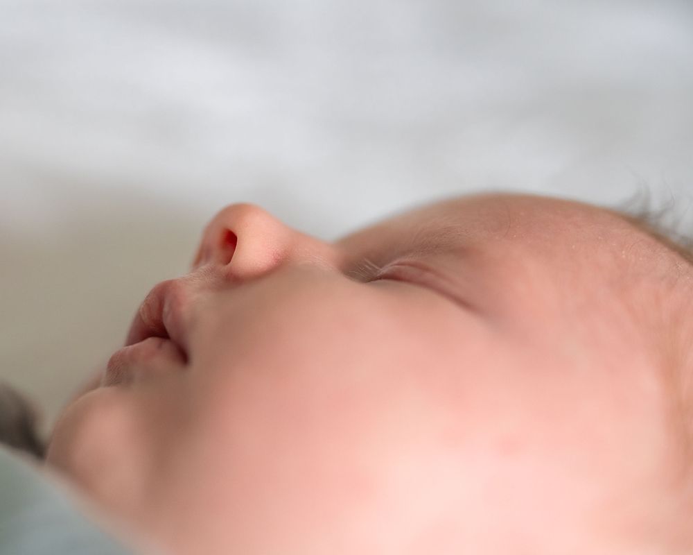 Close-up profile view of a sleeping baby's face with soft, delicate features against a light background.