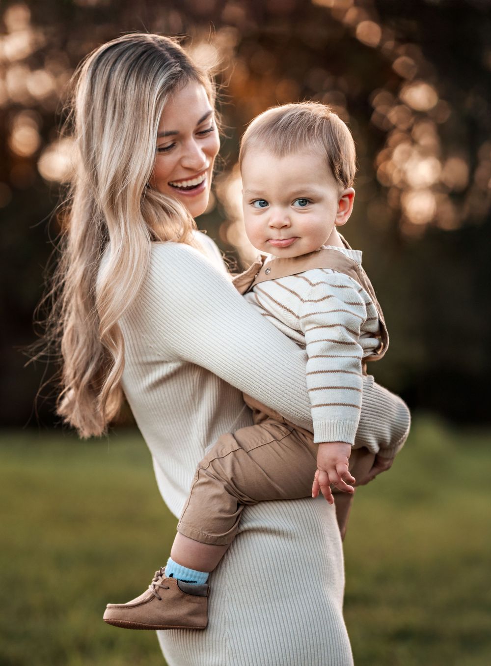 A delightful moment captured outdoors with warm sunlight as they share laughter and smiles in matching neutral tones.