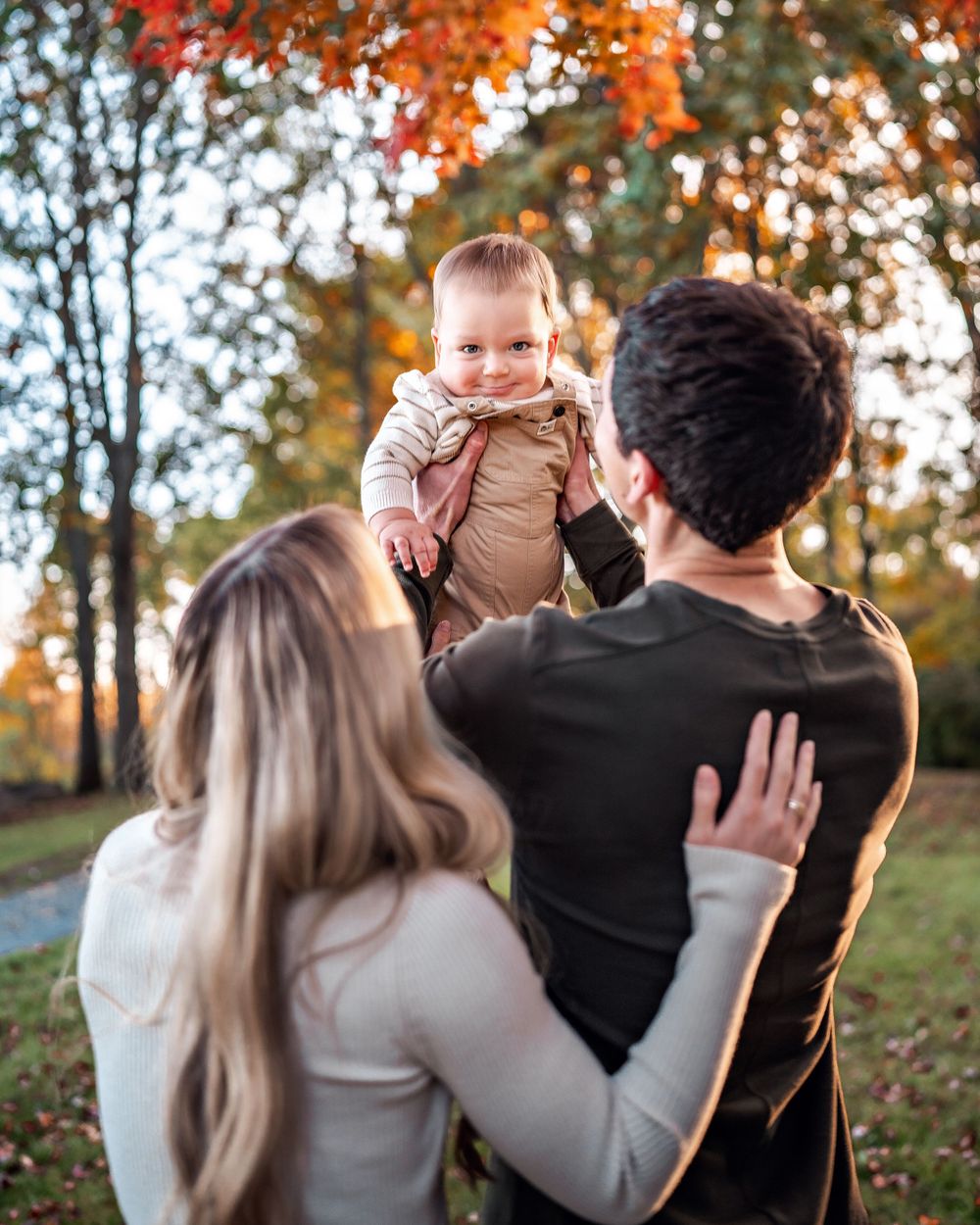A family stands together during autumn, surrounded by colorful fall foliage in an outdoor park setting.