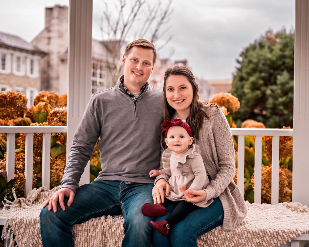 A family sits together on a bench for an autumn outdoor portrait with orange foliage in the background.