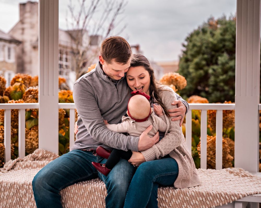 A cozy family portrait on a porch swing during autumn with orange trees in the background.