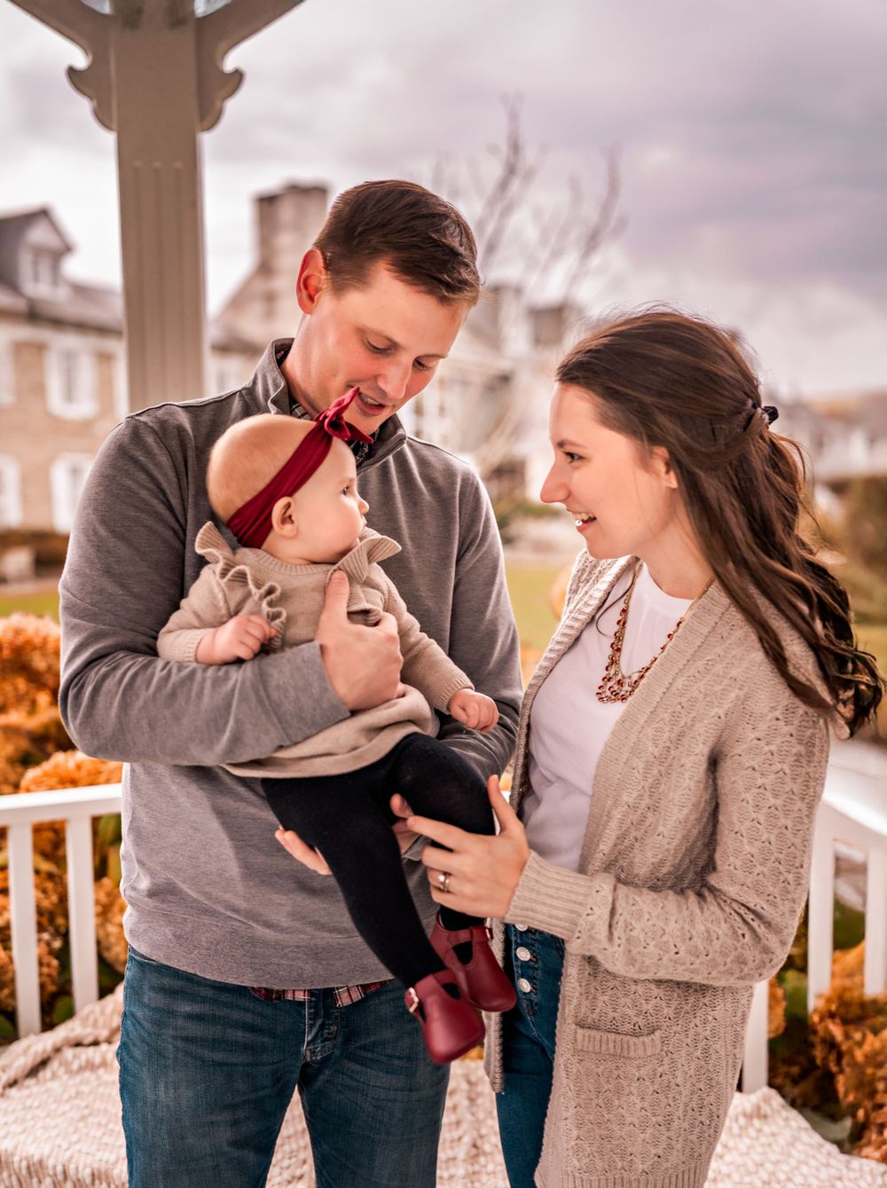 A family shares a tender moment together on an autumn porch with fall foliage in the background.