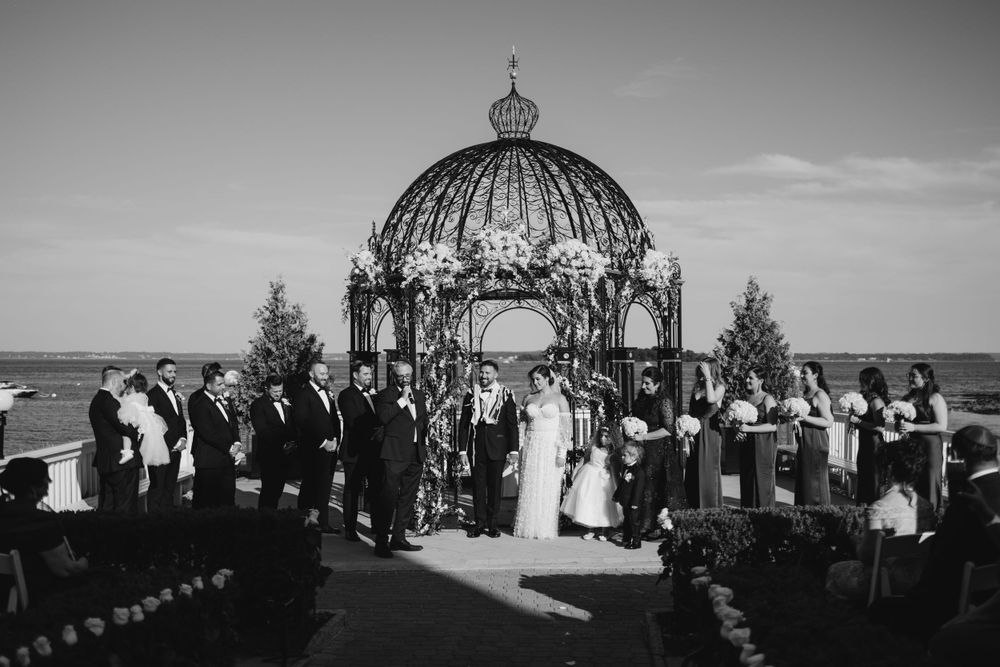 Black and white wedding ceremony taking place under an ornate domed gazebo overlooking the ocean.