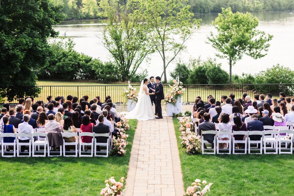 A beautiful outdoor wedding ceremony overlooking a lake with white chairs set up on a manicured lawn and stone pathway.