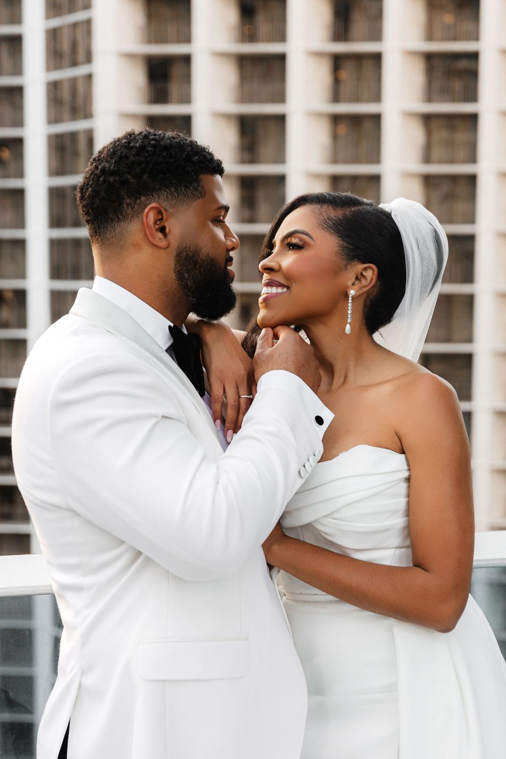 A romantic wedding portrait shows a couple in white formal attire gazing lovingly at each other.