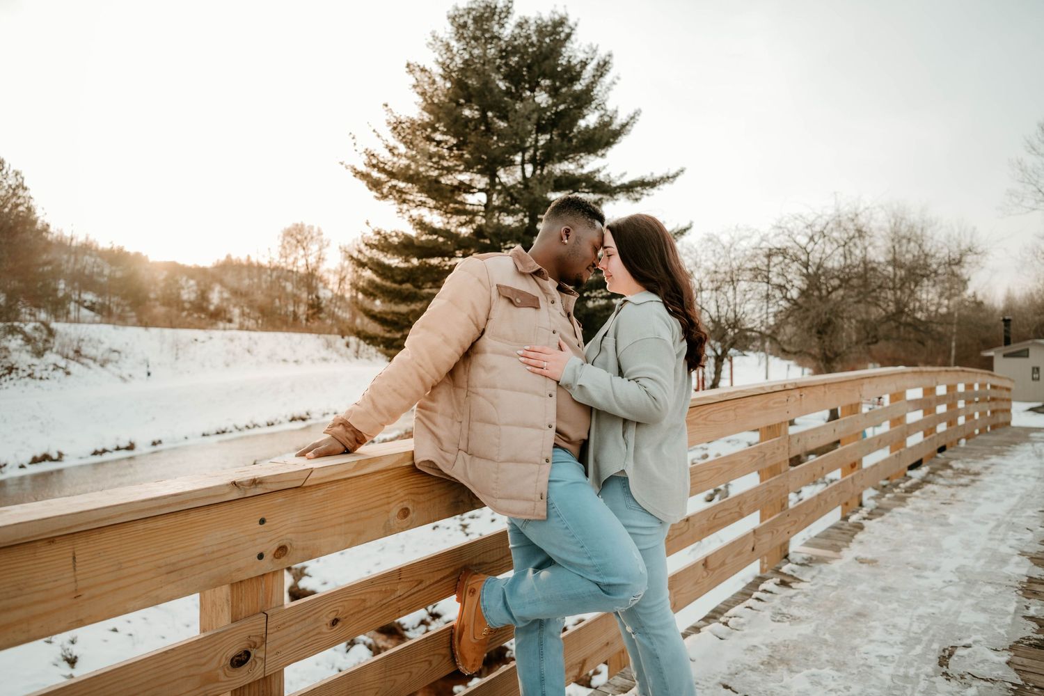 Couple sharing intimate moment on wooden bridge during winter with snowy landscape.