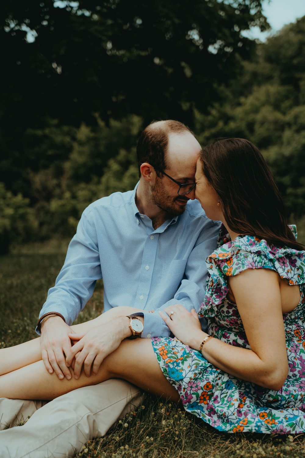 Couple sitting together on grass, sharing a romantic moment in a lush green outdoor setting.