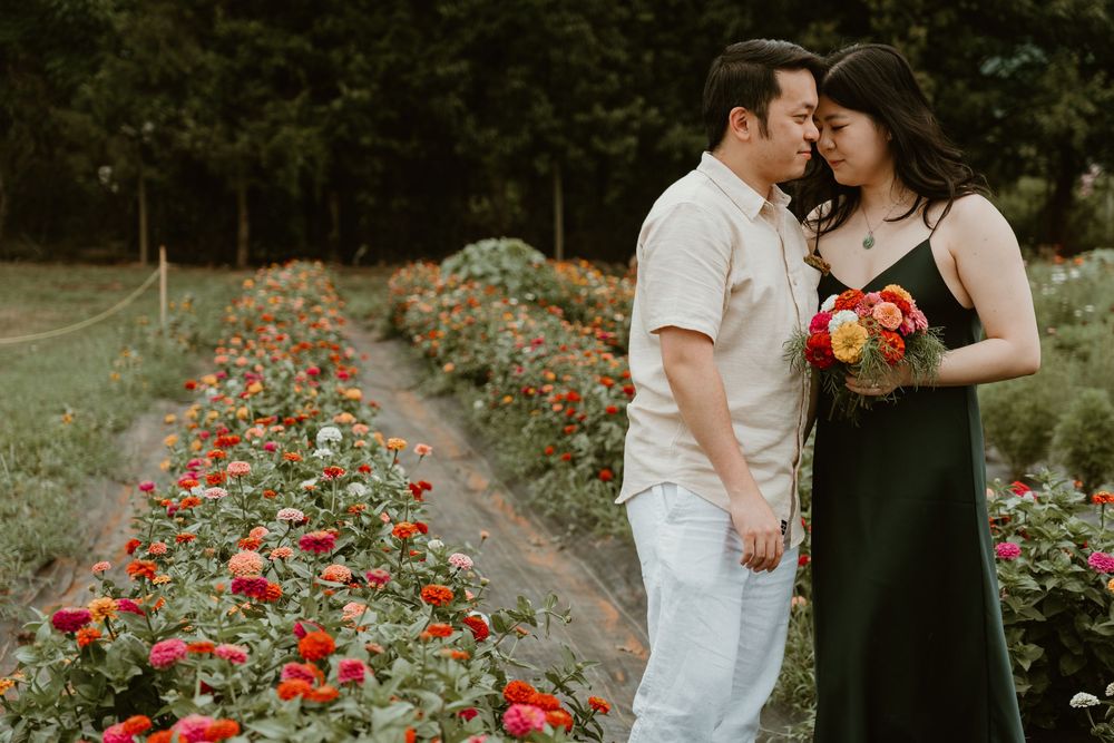 Couple sharing a romantic moment in a colorful flower garden, woman holding a bouquet of red and orange blooms.