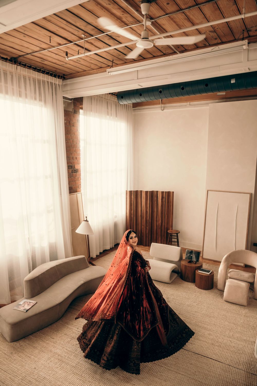 A flowing black and coral-colored gown twirls gracefully in a modern minimalist room with white curtains and wooden beams.